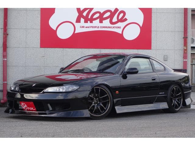 Sleek black Nissan Silvia S15 with custom wheels parked in front of a red sign.