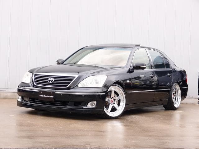 Lowered black Toyota Celsior luxury sedan with aftermarket silver five-spoke wheels on wet pavement.