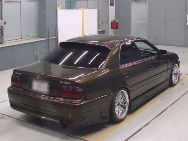 Modified dark green Toyota Chaser sedan with silver wheels and tinted windows indoors.