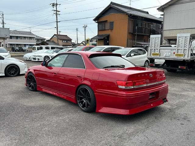A modified red Toyota sedan with black wheels parked in a Japanese car lot.