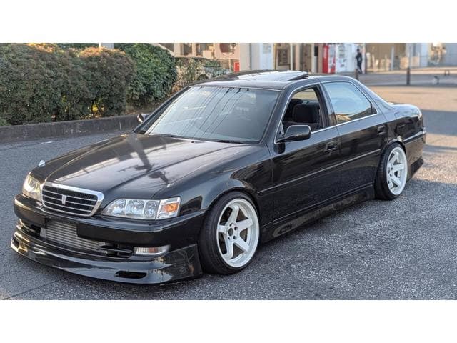 Lowered black Toyota Cresta sedan with white five-spoke wheels parked on a city street.