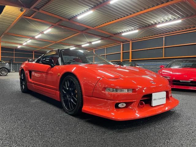 Sleek red Honda NSX sports car with black wheels parked inside a brightly lit garage.