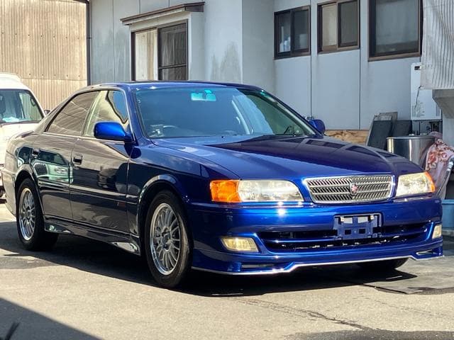 Polished blue Toyota Chaser sedan with silver wheels parked in front of a building.