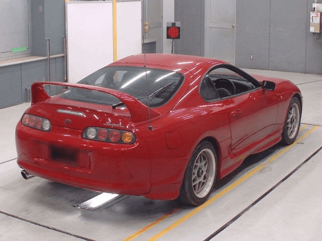 Red Toyota Supra sports car with a large rear wing parked in an indoor garage.